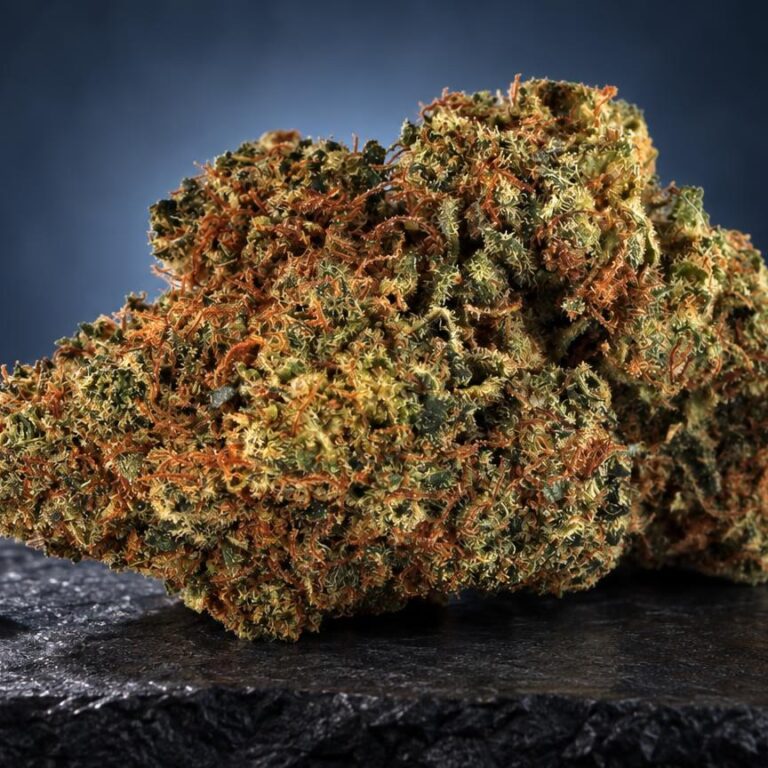 Diamond Kush com estrutura densa e ramificada, tons verde-dourados e laranja, acompanhado de sementes ao lado