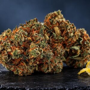 Flor de cannabis Super Lemon Haze com tons verde-alaranjados e tricomas brilhantes, ao lado de casca de limão