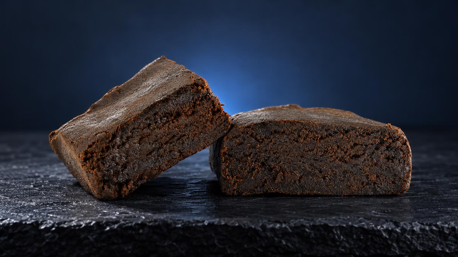 Dois blocos compactos de Tipos de haxixe com textura granulosa castanha, sobre superfĂcie escura
